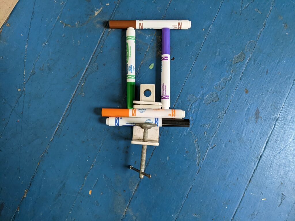 Current image: markers placed to make a rectangle and a screw as well on a blue background.